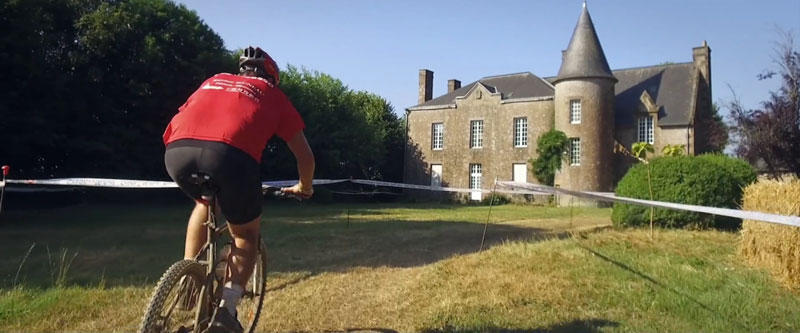 un homme de dos fait du vélo en direction d'un manoir le tout dans un cadre bucolique