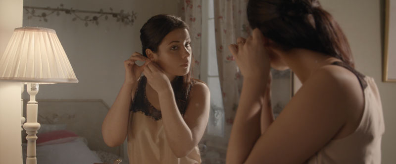 Femme un miroir met une paire de boucles d'oreilles du Joaillier Frédéric Parisse